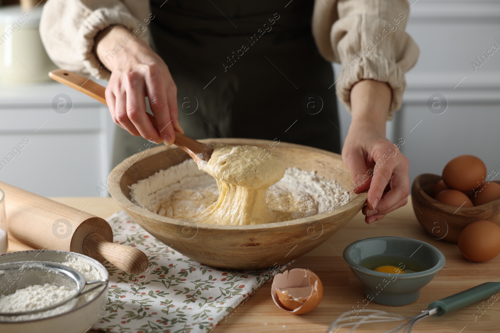 Photo of Woman kneading dough with spoon in bowl at wooden table indoors, closeup