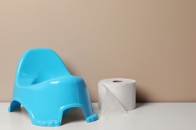 Photo of Light blue baby potty and toilet paper on white table near brown wall, space for text