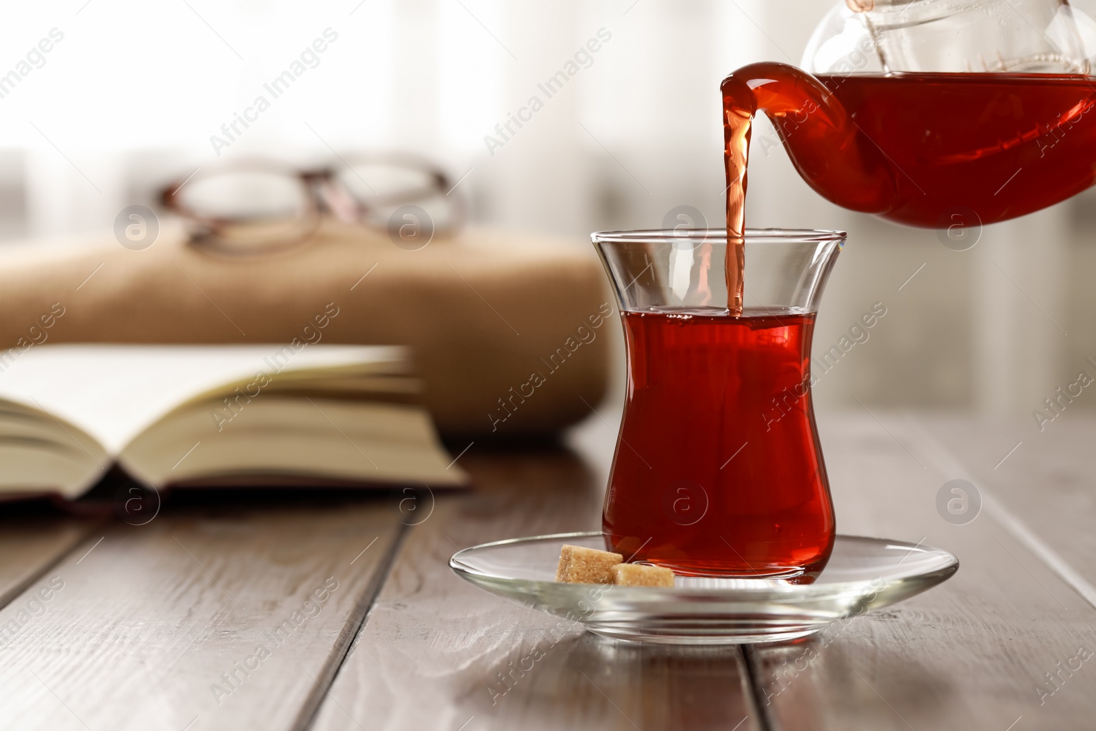 Photo of Pouring traditional Turkish tea from pot into glass on wooden table, space for text