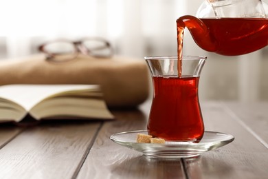 Pouring traditional Turkish tea from pot into glass on wooden table, space for text