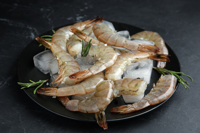 Photo of Fresh raw shrimps with rosemary and ice cubes on black table
