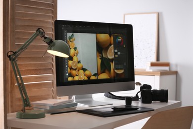 Photo of Retoucher's workplace. Computer with photo editor application, camera and graphic tablet on table in office