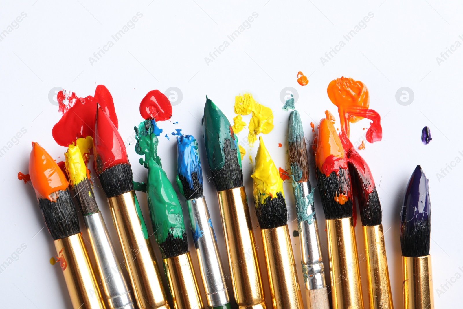 Photo of Brushes with colorful paints on white background, closeup