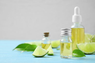 Photo of Lime essential oil and cut citrus fruits on light blue wooden table