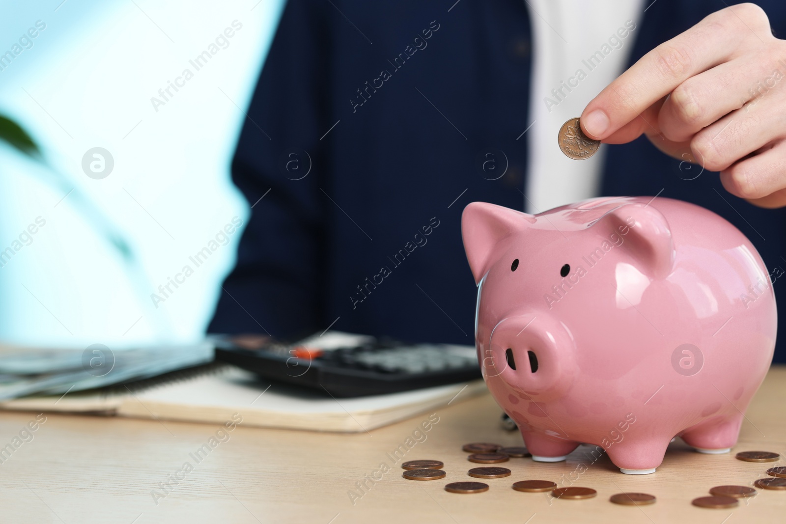 Photo of Financial savings. Man putting coin into piggy bank at wooden table, closeup