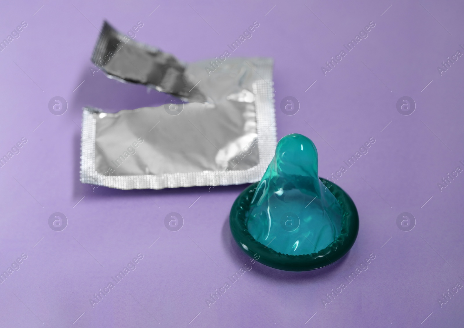Photo of Unpacked green condom and torn package on light purple background, closeup. Safe sex