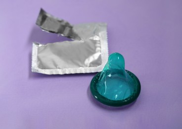 Unpacked green condom and torn package on light purple background, closeup. Safe sex