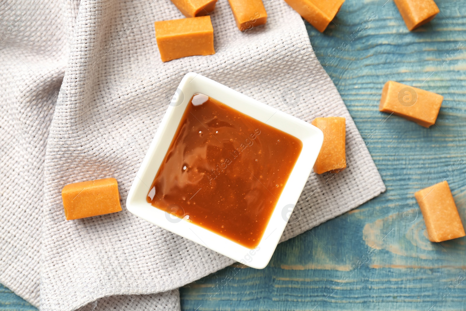 Photo of Delicious caramel candies and sauce on wooden background