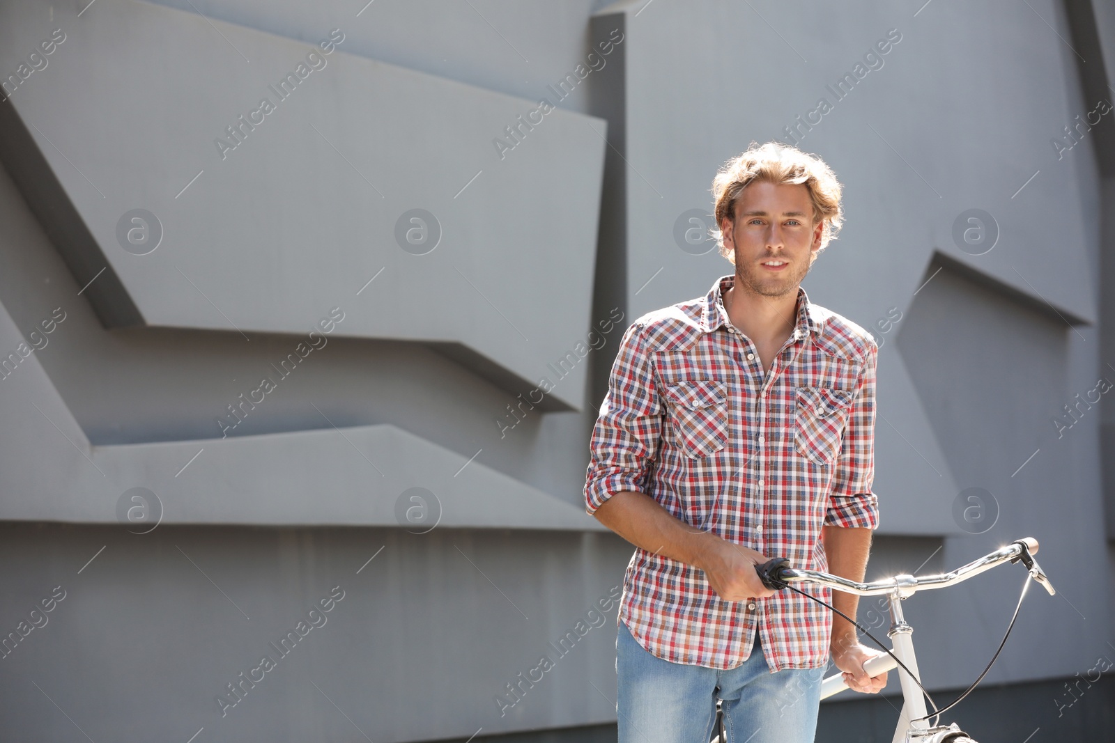 Photo of Handsome young man with bicycle near gray wall outdoors. Space for text