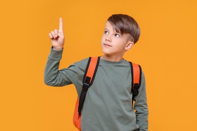Cute schoolboy pointing upwards on orange background