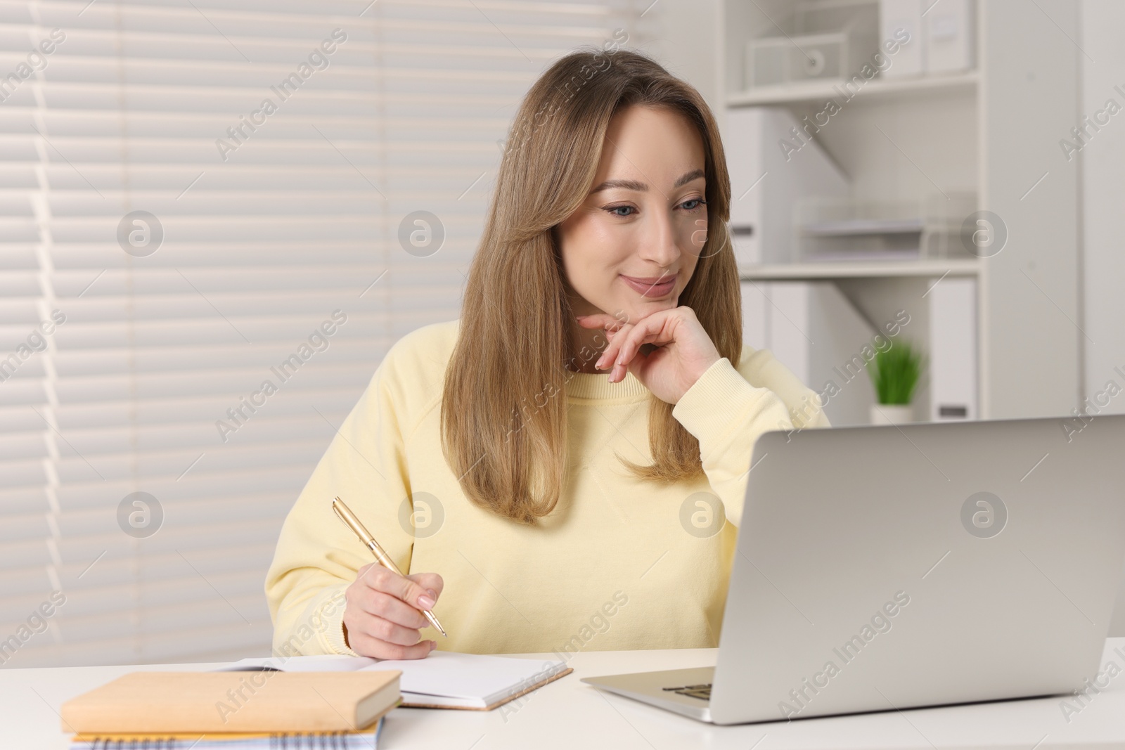 Photo of Young woman having video chat via laptop at white table indoors