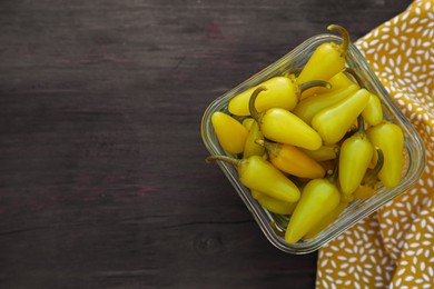 Photo of Bowl of pickled yellow jalapeno peppers on wooden table, top view. Space for text