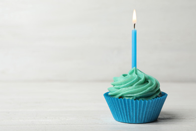 Delicious birthday cupcake with cream and burning candle on white wooden table. Space for text