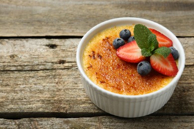 Delicious creme brulee with berries and mint in bowl on wooden table, closeup. Space for text