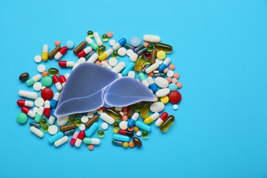 Photo of Paper liver and pills on light blue background, flat lay with space for text. Hepatitis treatment