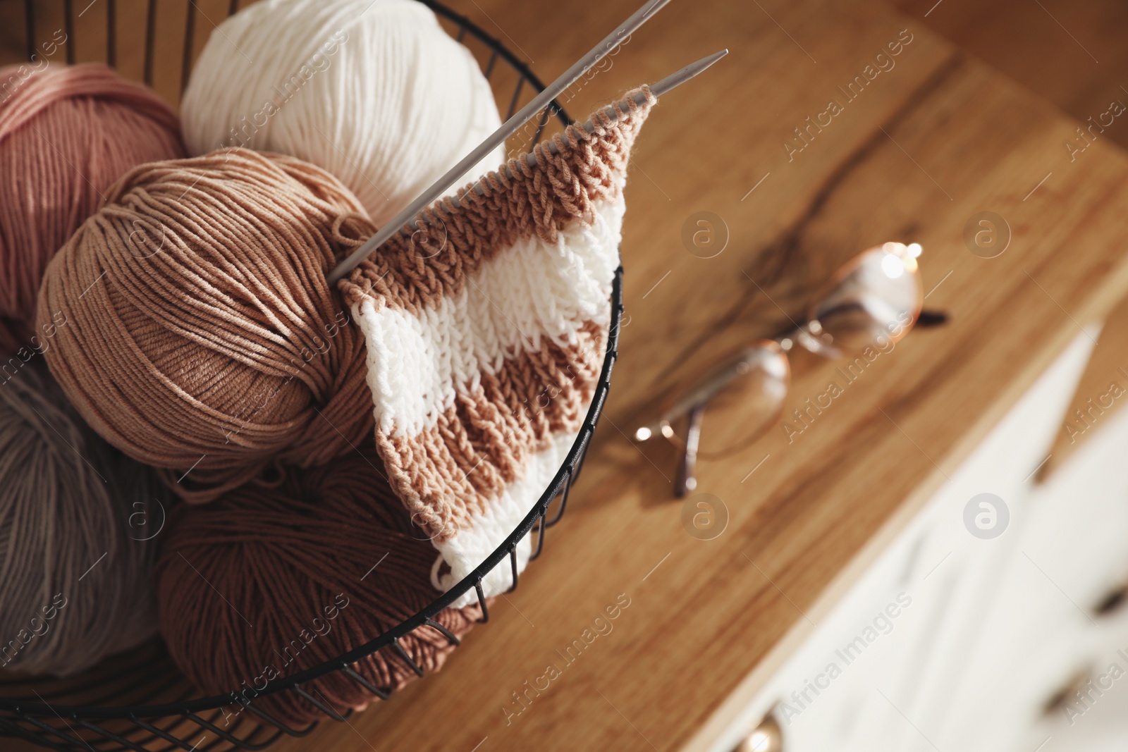 Photo of Yarn balls and knitting needles in metal basket on wooden table, closeup with space for text. Creative hobby