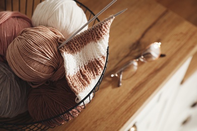 Photo of Yarn balls and knitting needles in metal basket on wooden table, closeup with space for text. Creative hobby