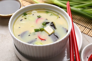 Bowl of delicious miso soup with tofu served on light grey table, closeup