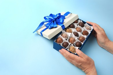 Photo of Woman with box of delicious chocolate candies on light blue background, closeup. Space for text