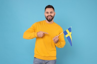 Photo of Young man holding flag of Sweden on light blue background