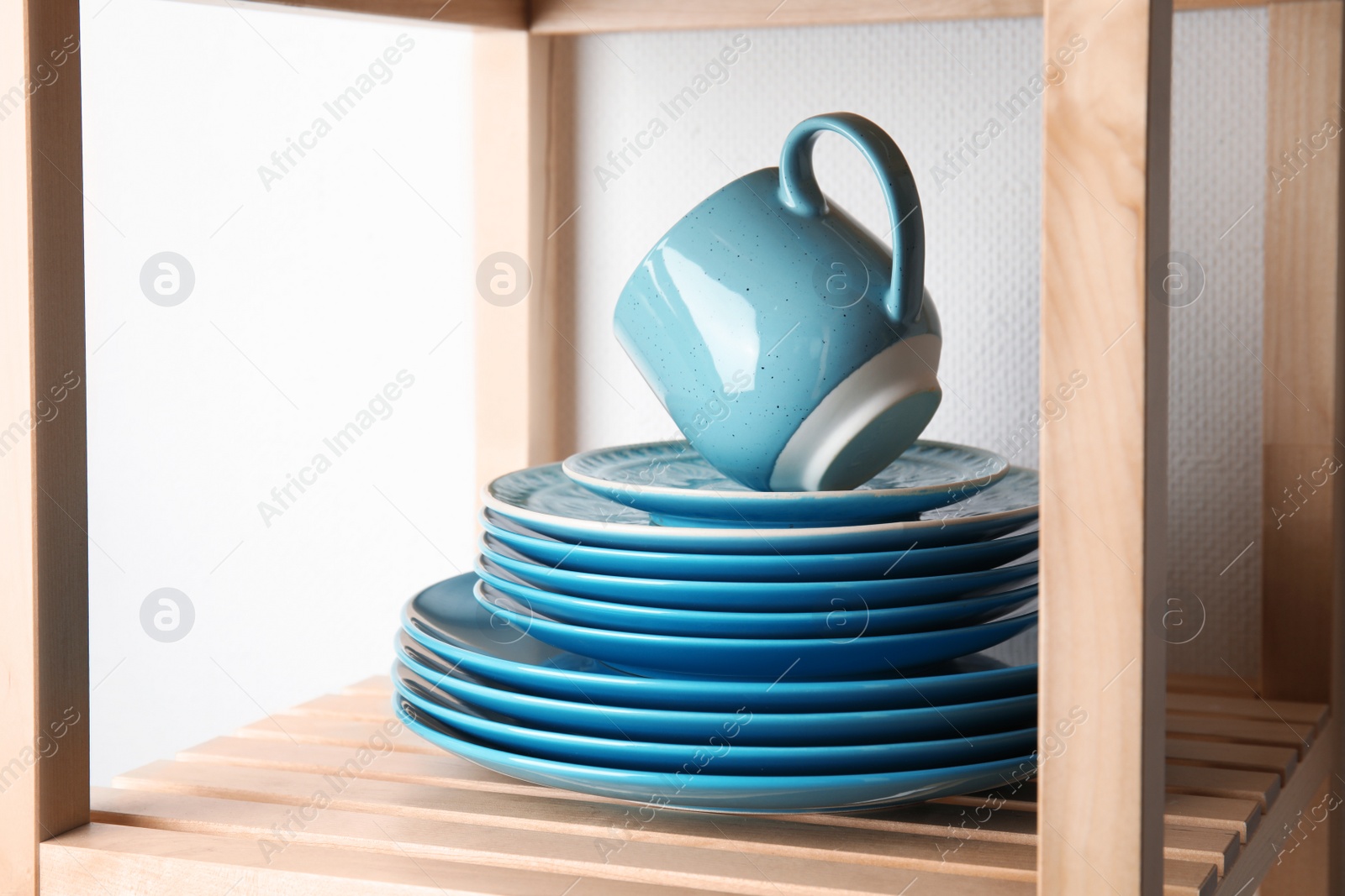 Photo of Set of dinnerware on wooden shelf against light background. Interior element