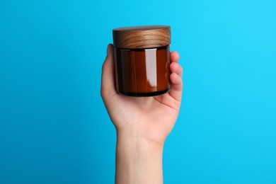 Woman holding jar of face cream on light blue background, closeup