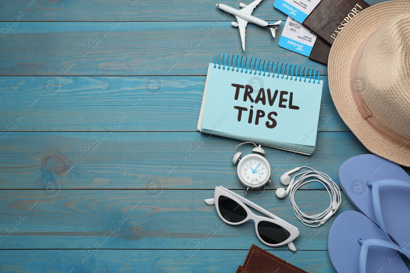 Photo of Notebook with phrase Travel Tips and tourist items on light blue wooden table, flat lay. Space for text