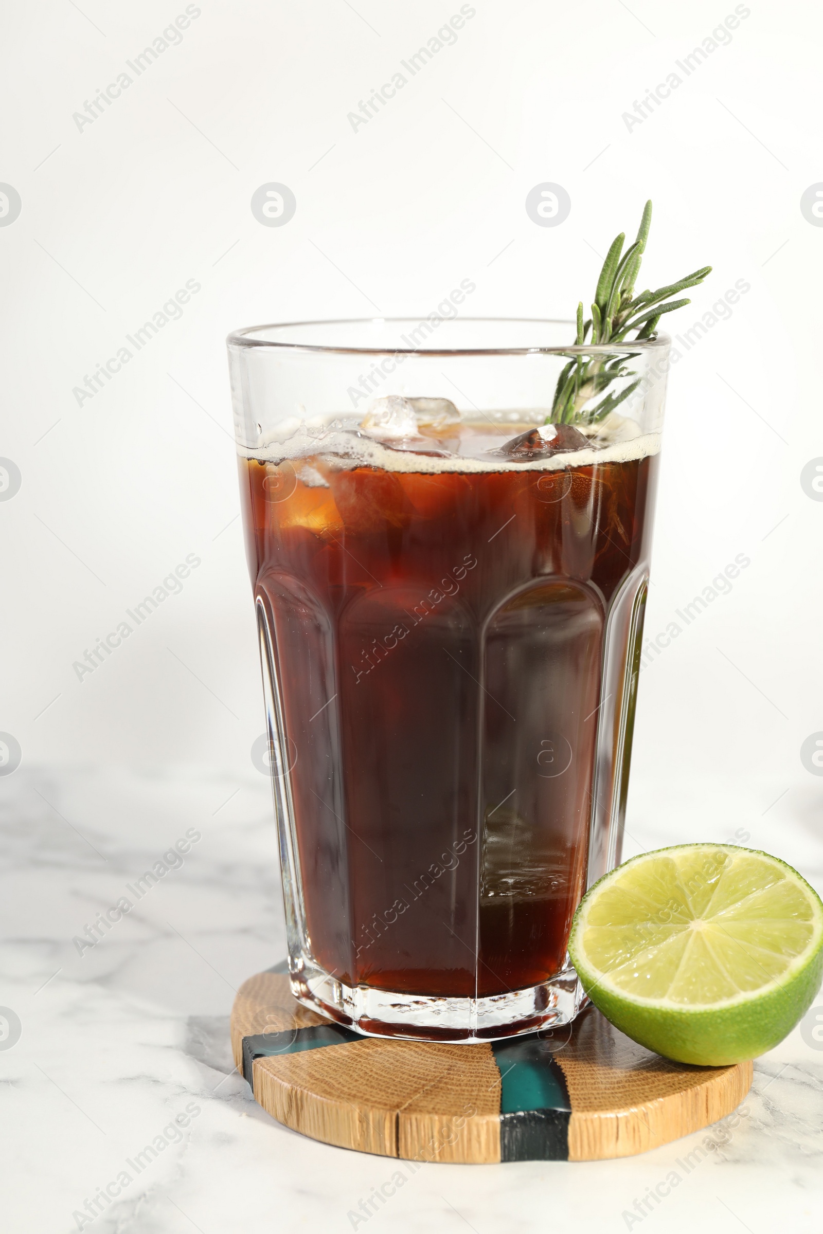 Photo of Refreshing iced coffee with rosemary in glass and fresh lime on white marble table