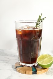 Photo of Refreshing iced coffee with rosemary in glass and fresh lime on white marble table