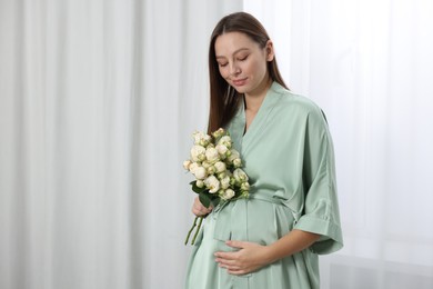 Photo of Beautiful pregnant woman with bouquet of roses near window indoors, space for text