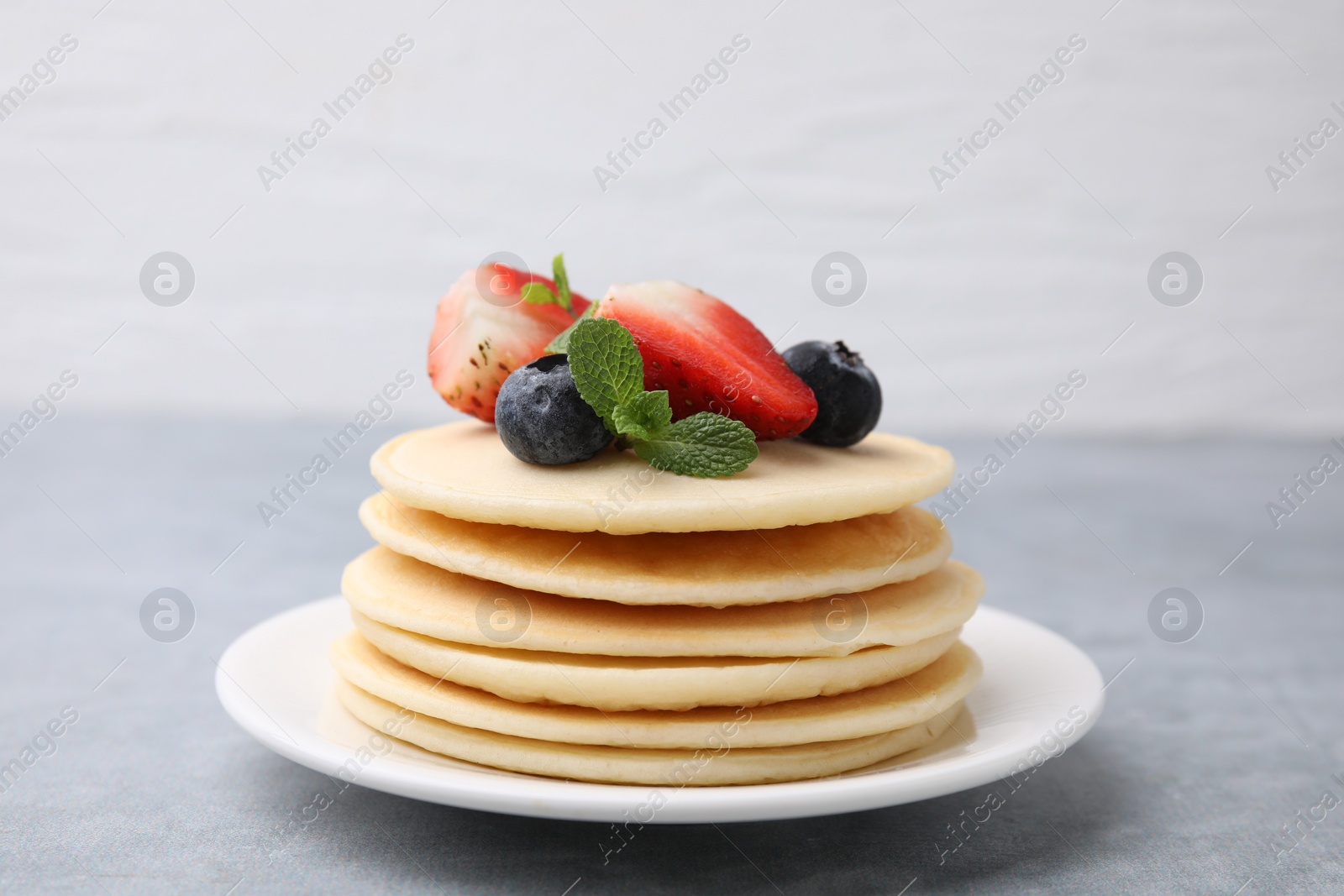 Photo of Stack of tasty pancakes with fresh berries and mint on light grey table, closeup