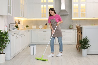 Happy woman cleaning floor with mop in kitchen