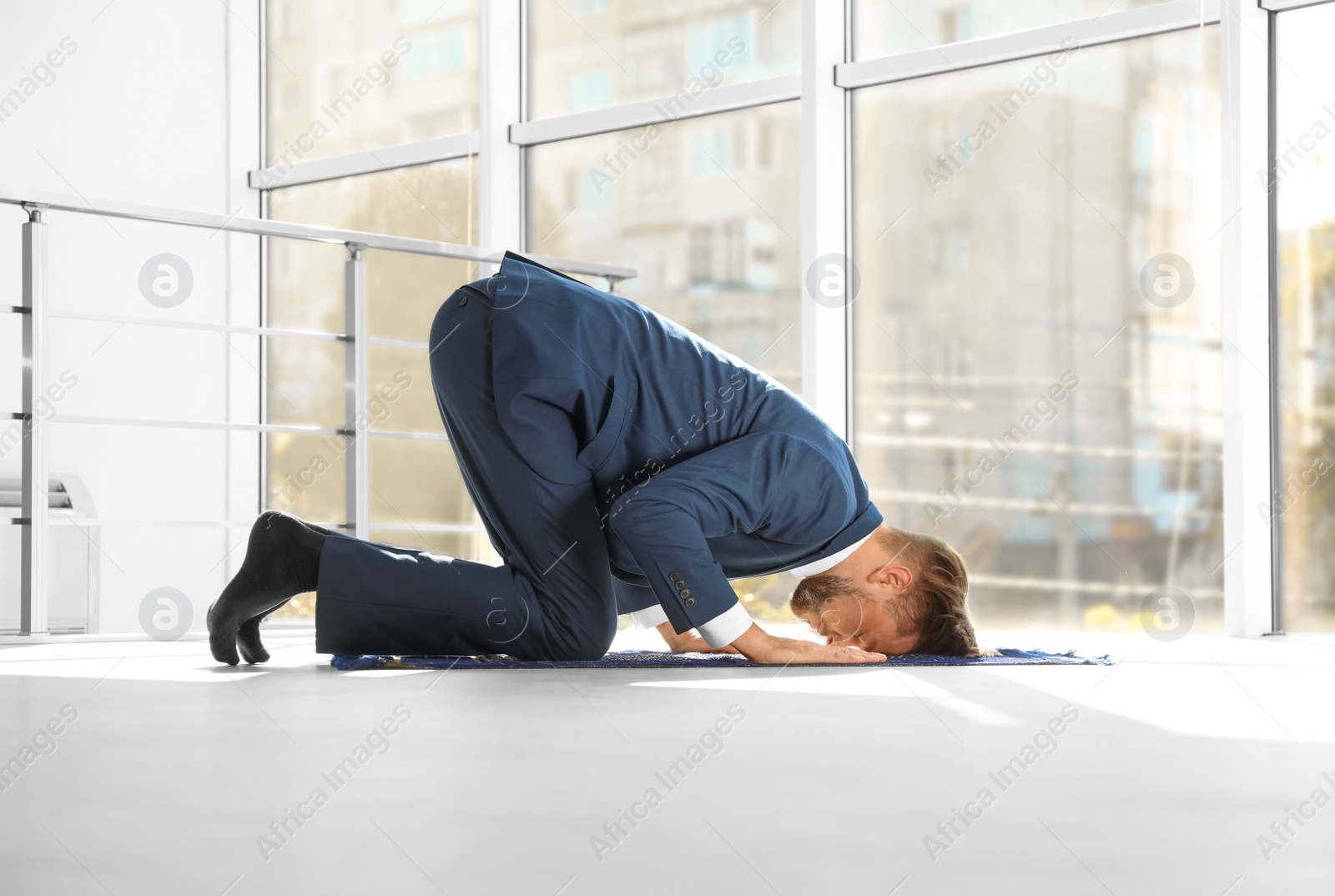 Photo of Muslim man in suit praying on rug indoors