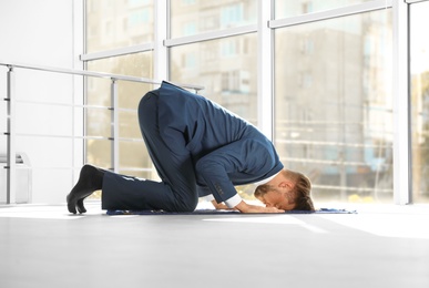 Muslim man in suit praying on rug indoors