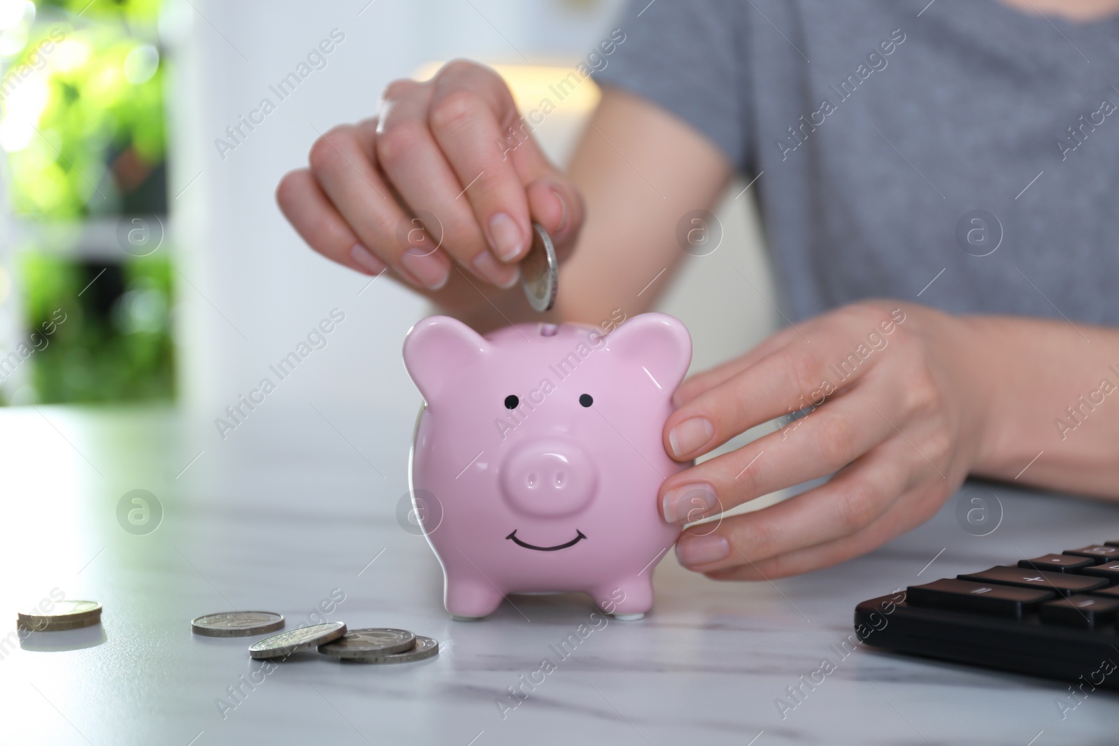 Photo of Woman putting money into piggy bank at marble table indoors, closeup