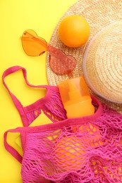 Photo of String bag with beach accessories and oranges on yellow background, flat lay