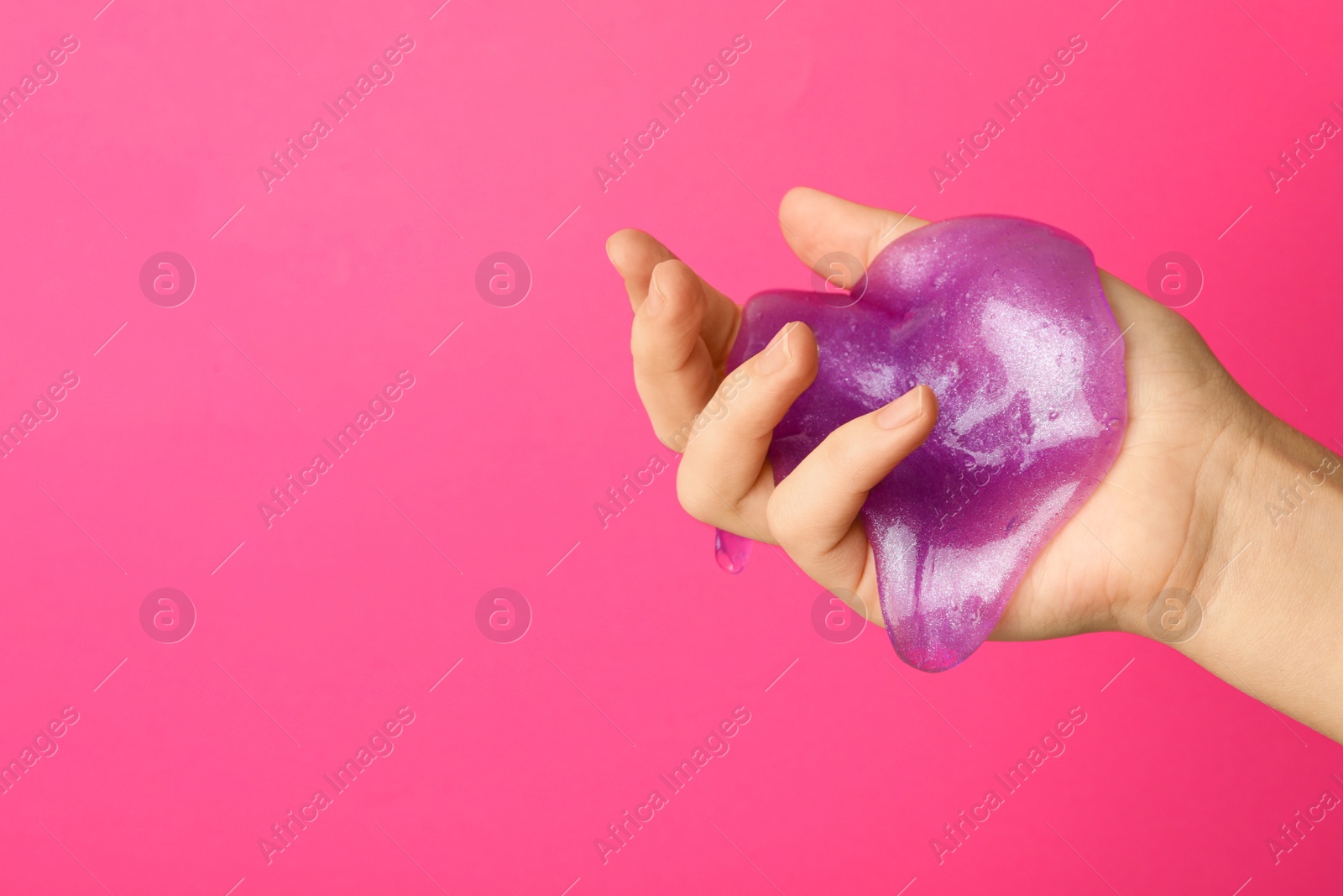 Photo of Woman playing with purple slime on pink background, closeup. Antistress toy