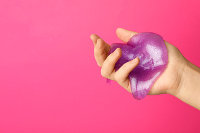 Photo of Woman playing with purple slime on pink background, closeup. Antistress toy