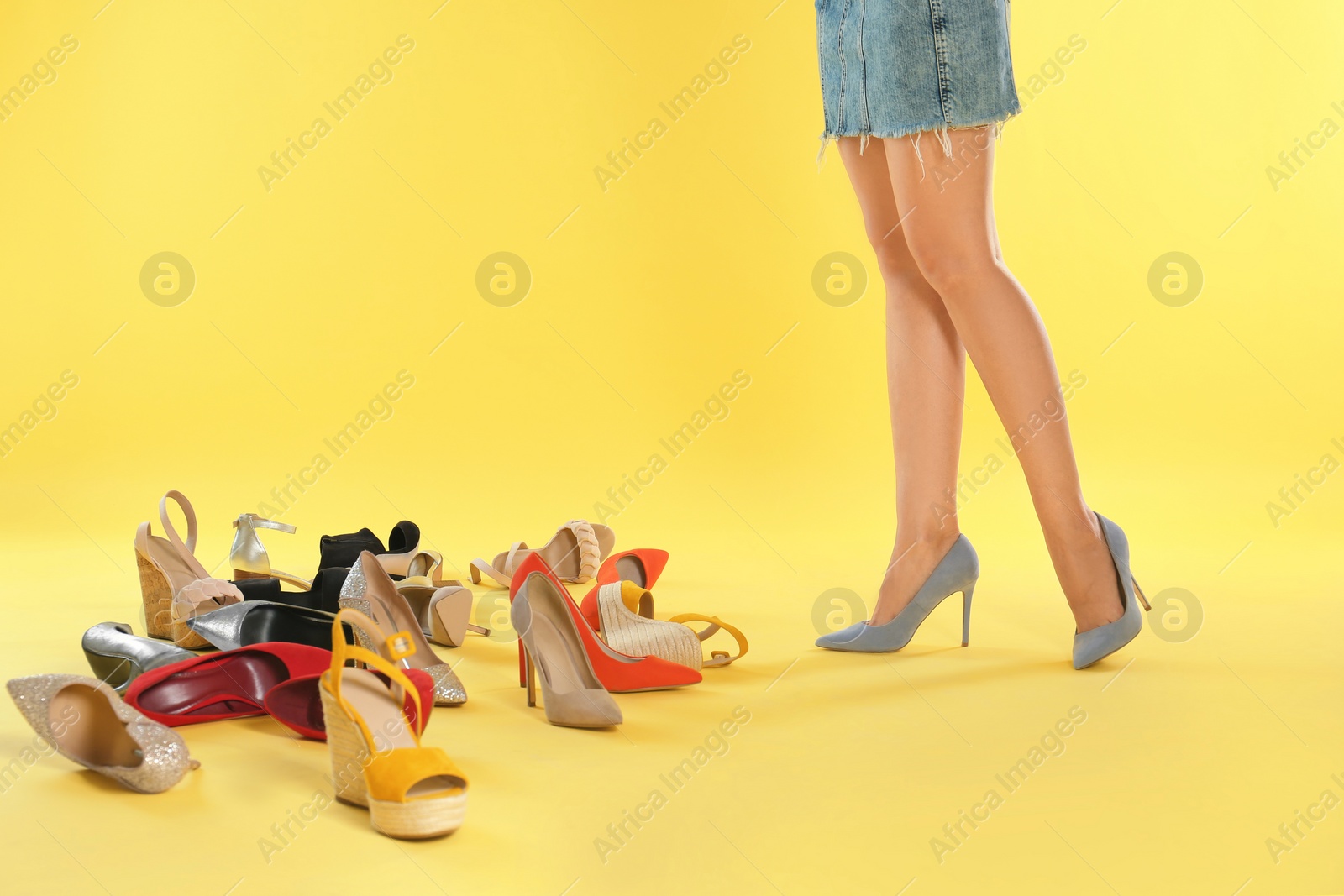 Photo of Woman trying on different high heel shoes on yellow background, closeup