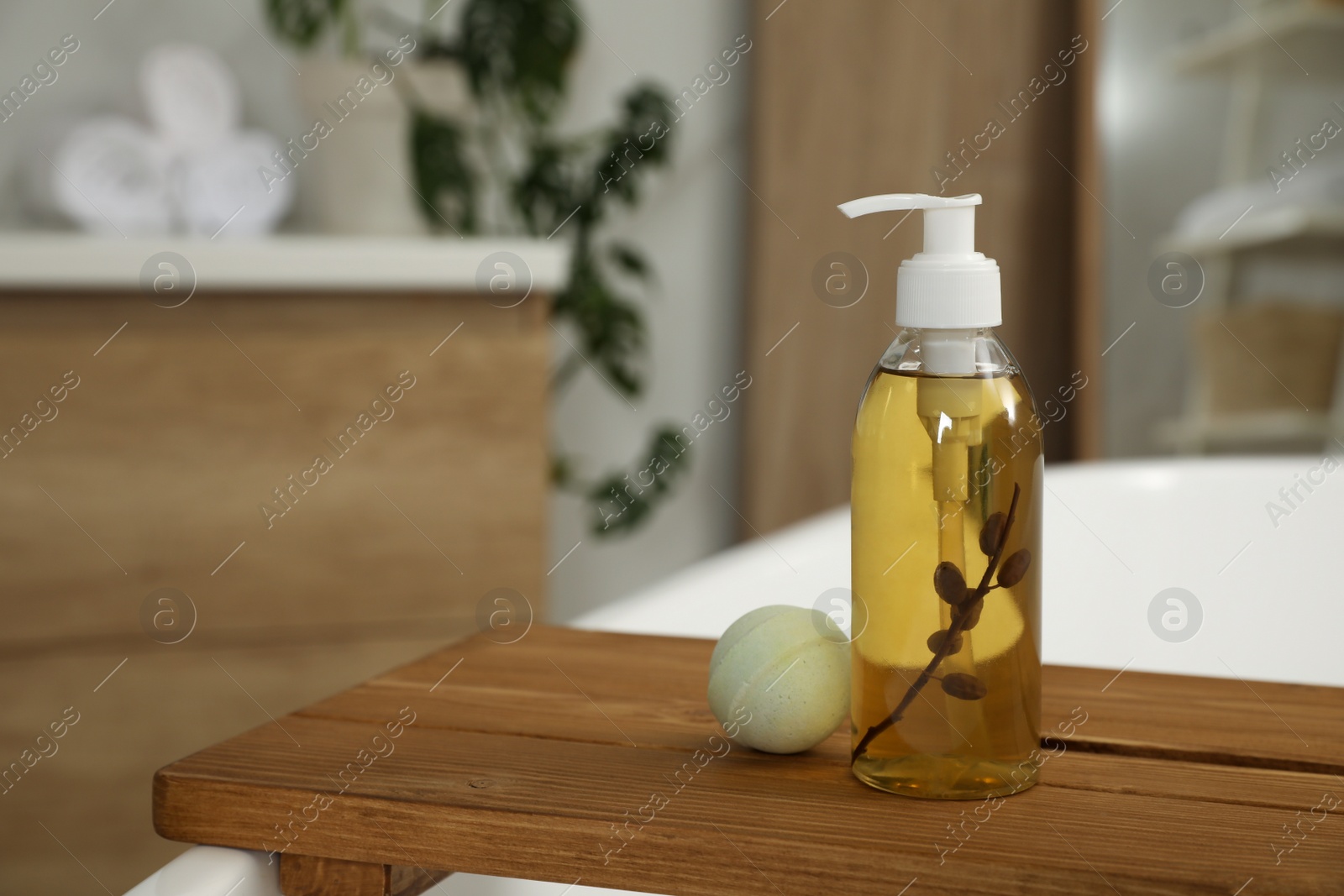 Photo of Wooden tray with bottle of shower gel and bath bomb on tub indoors, space for text