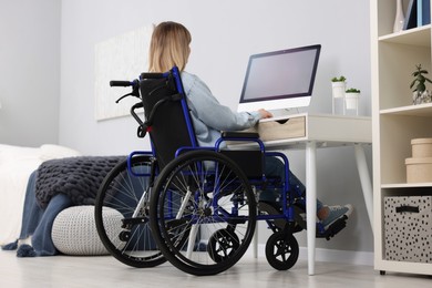 Woman in wheelchair using computer at table in home office