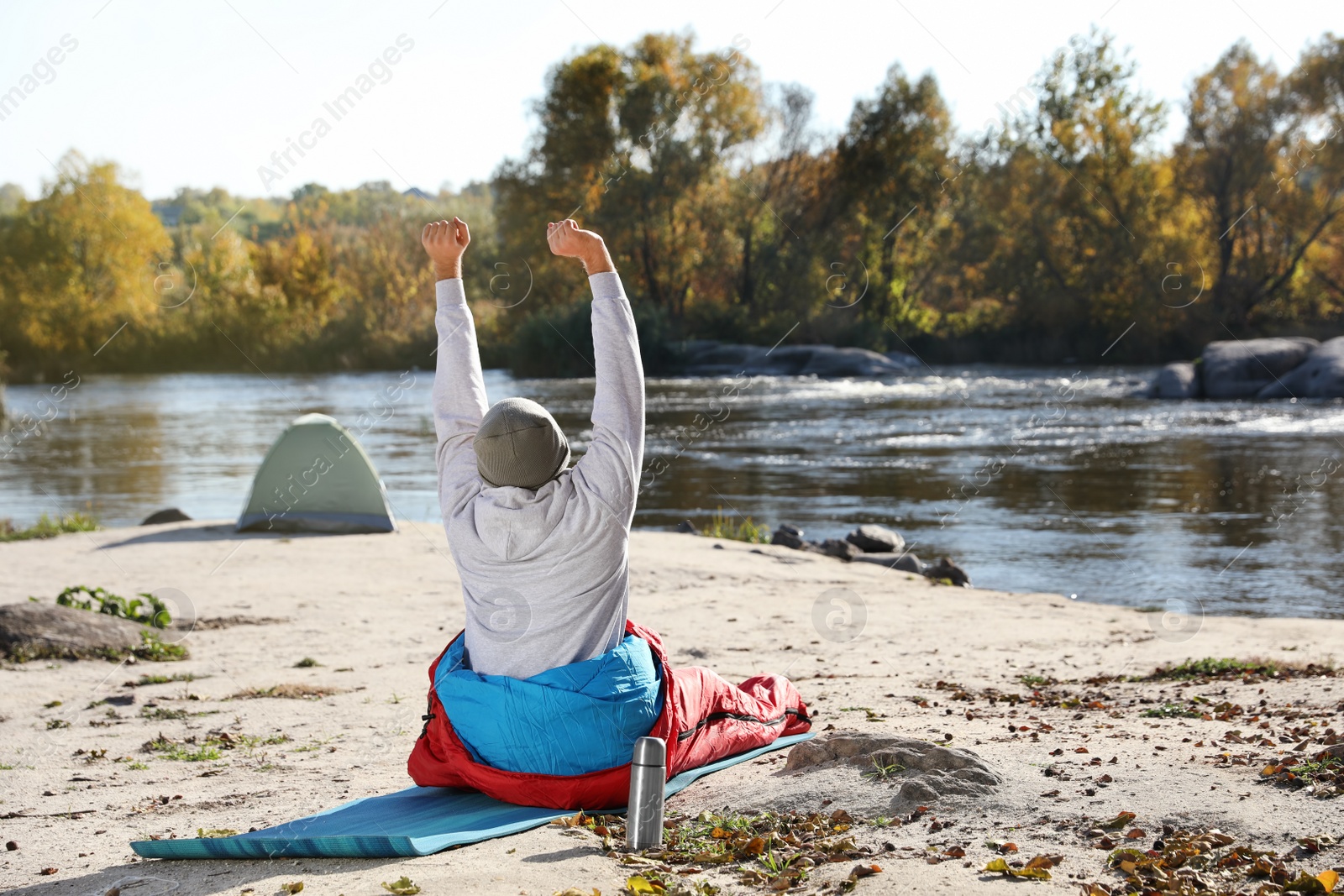 Photo of Male camper stretching in sleeping bag on wild beach. Space for text