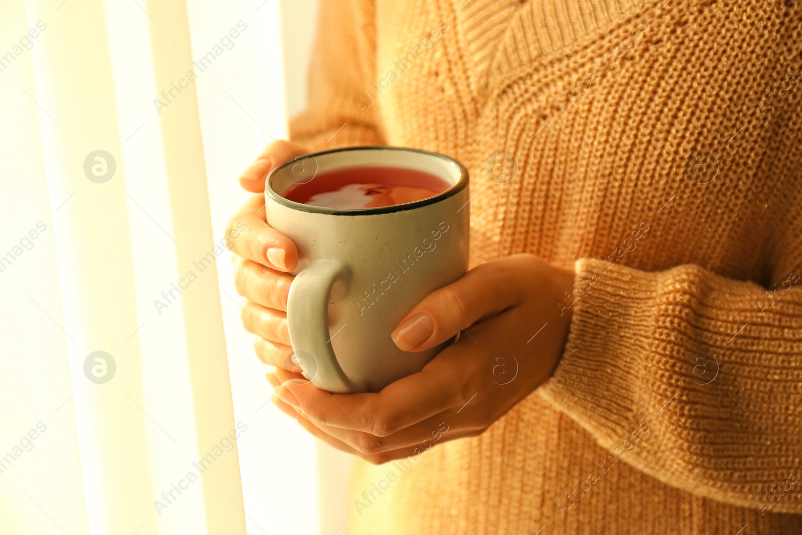 Photo of Woman holding elegant cup with tea near window indoors, closeup