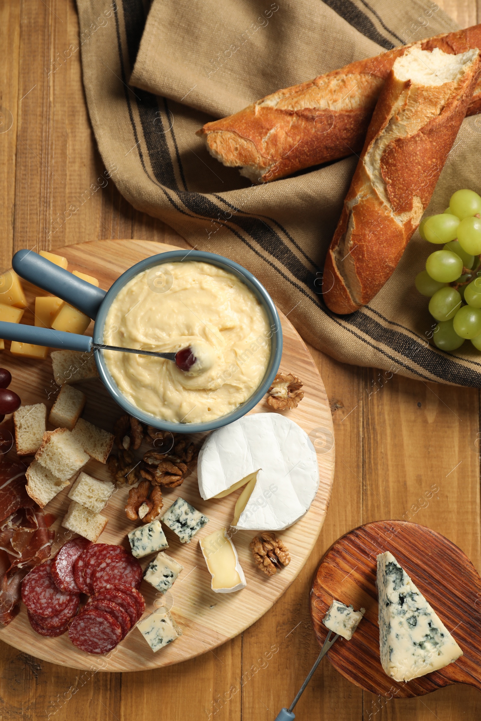 Photo of Fondue pot with tasty melted cheese, forks and different snacks on wooden table, top view