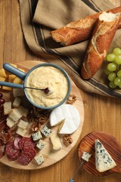 Photo of Fondue pot with tasty melted cheese, forks and different snacks on wooden table, top view