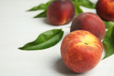 Photo of Fresh peaches and leaves on white table, space for text