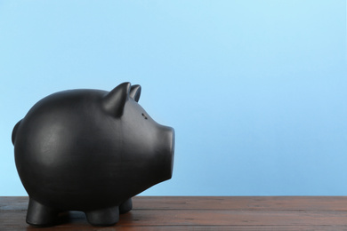 Photo of Black piggy bank on wooden table against light blue background. Space for text