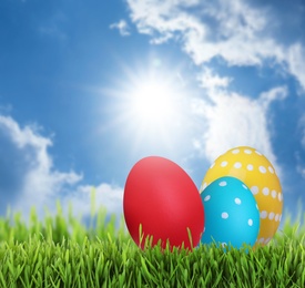 Image of Bright Easter eggs on green grass outdoors, space for text 