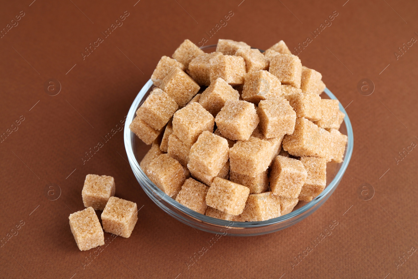 Photo of Brown sugar cubes in bowl on color background, closeup