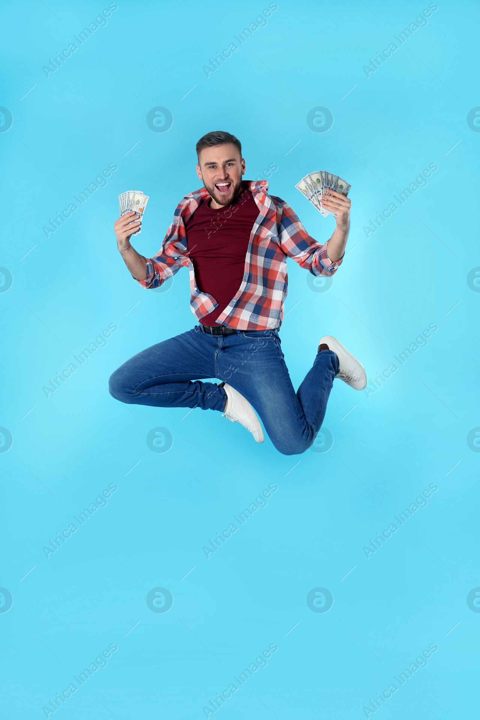 Photo of Happy young man with money jumping on color background. Space for text